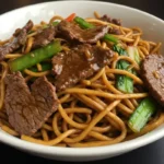 A steaming bowl of Mongolian beef noodles with beef, noodles, and sesame seeds